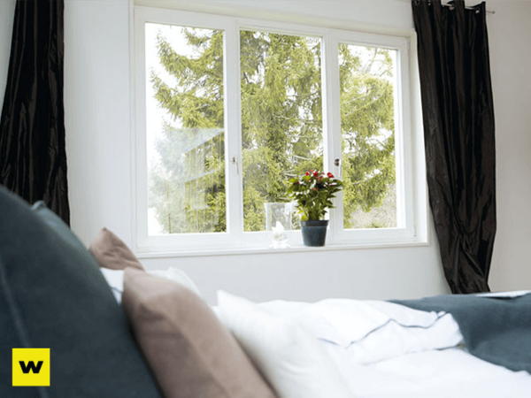 Helles Schlafzimmer mit großem Fenster, Blick ins Grüne und Zimmerpflanze auf Fensterbrett.