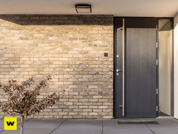 Moderne Haustür aus dunklem Material mit Glaseinsatz vor heller Klinkerfassade.