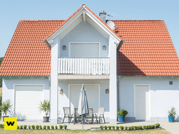 Modernes Einfamilienhaus mit rotem Satteldach, Terrasse und geschlossenen Rollläden.